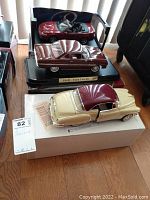 Three die cast car models displayed together: red 2003 Mustang Cobra, brown 1963 Falcon on black base, cream/maroon 1950 Chevy on white box.