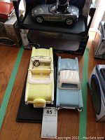 Three die cast car models displayed on black base: yellow 1957 Chevrolet Bel Air convertible, blue and white convertible with removable roof, and silver BMW Z4 model on top of box.