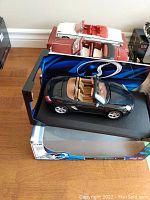 Black Porsche Boxster S die cast model car in 1:18 scale with tan interior inside original display box placed on the floor.