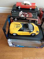 Photo of three die cast model cars displayed on their black bases including a red and white 1957 Plymouth, a black and red 1958 Citations convertible, and a yellow Lamborghini roadster.