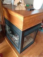 Side angled view of electric fireplace showing wooden mantel and glass front with simulated logs inside.