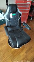 Front view of black and silver X-Rocker gaming chair showing cushioned backrest and seat with armrests.