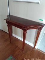 Wooden hall table in dark brown finish with tapered legs, decorative curved front edges, and carved details beneath the drawer.