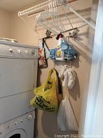 Washer and dryer unit with metal shelf above holding hangers and cleaning products, iron hanging on wall.