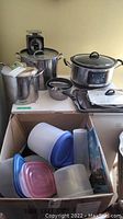 Hamilton Beach slow cooker, stainless steel pots and lids, Pelouze kitchen scale, plastic storage containers in box, cookie sheets stacked