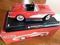 Front side view of the red and white 1958 Chevrolet Corvette die cast model on display base with original box.