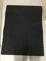 Full view of one black outdoor carpet showing rectangular textured pattern.