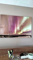 Photo of the 20x30 signed limited edition photo of the Northern Lights mounted on a wall over a desk with pens and a cup.