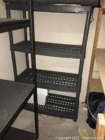 Full view of the black resin shelving unit with 4 perforated shelves and vertical support legs.