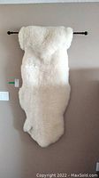 Front view of deep pile white sheepskin hanging on rod against wall