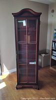 Front view of the tall three-side glass display cabinet showing glass door, mahogany wood frame, and arched crown top.