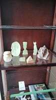Seven Egyptian-themed stone figures of various sizes and materials displayed in a glass shelf.