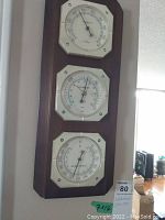 Full view of the wooden framed weather station showing the three instruments stacked vertically: thermometer on top, barometer in the middle, and hygrometer at the bottom.