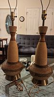 Pair of 1960s vintage genie lamps with tall, textured, bottle-shaped bodies and brass bases, placed on a glass table in a living room setting.