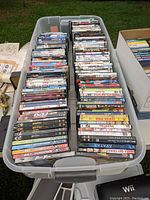 Plastic box filled with assorted DVDs and VHS tapes arranged in rows showing titles like Avatar, Fast & Furious.