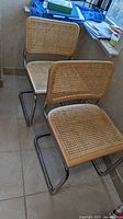 Front view of two vintage Cesca cantilever chairs showing cane seats and backs, and tubular chrome frames.
