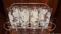 Full view of eight vintage Libbey glass tumblers decorated with white rose patterns, placed neatly in a vintage metal carrying tray with handles on either side.