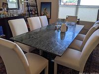Full view of green marble dining table surrounded by chairs in dining room setting.