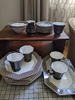 Image showing stacked plates, cups, and bowls arranged on table highlighting geometric patterned rims and octagonal shapes.