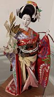 Full view of the geisha doll showing the colorful kimono, hairstyle, and the branch in hand.