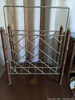 Front view of a mid century modern magazine rack showing brass lattice structure and wooden legs with brass finials.