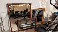 Three wood-framed mirrors leaning against a wall with visible hanging hardware and wires