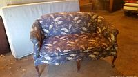 Front view of Victorian style settee showing floral upholstery and curved wooden legs.
