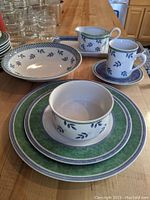 Photo of stacked plates, bowls, coffee cup and gravy boat highlighting the blue leaf motif and green borders.