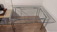 Full view of rectangular glass top dining table on chrome tubular base, showing clear thick glass and base structure.