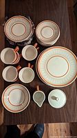 Top down view of entire dinnerware set including plates, mugs, creamer, and sugar bowl on a wood table.