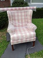 Front view of wingback chair showing white and rose plaid upholstery and walnut legs, chair wrapped in plastic.