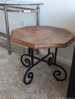 Wood and iron end table showing parquet octagonal wood top and black scroll iron base from side angle.
