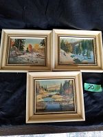 Three framed scenic lithographic prints with landscapes including autumn and snowy scenes, placed together on a dark surface.