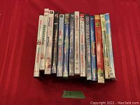 Photo of 15 DVDs arranged side by side showing the spines and titles against a red cloth background.