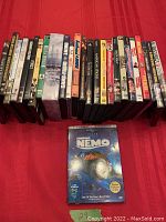 Overhead photo showing the DVD lot. One Finding Nemo 2 Disc Collector Edition DVD in front, and 25 additional DVDs arranged behind it in a row.