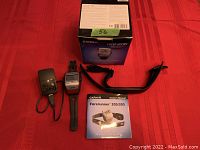 Photo shows Garmin Forerunner 305 wristwatch, heart rate monitor chest strap, charging power cord, owner's manual, and original box all arranged on red fabric.