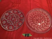 Two round glass serving platters on a red cloth background, showing detailed patterns of stars and leaves embossing on surface.