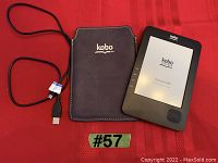 Photo of Kobo eReader, USB charging cable, and Kobo cover on red cloth background.