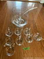 Photo of the entire punch bowl set placed on floor, showing the punch bowl, ladle inside the bowl, and 8 glasses arranged around it.