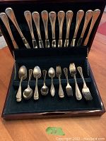 Opened wooden case showing full set of 11 Oneida Community silverware pieces arranged in green velvet slots including 3 knives, 3 dinner forks, 2 dessert forks, 2 spoons, and 1 teaspoon.