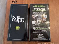Front and back view of the black box featuring The Beatles logo and a green apple graphic, listing contents including 13 original studio albums, Past Masters 2 CDs, and a mini documentaries DVD.