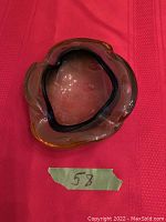 Top view of curved vintage glass ashtray with green trim on red fabric, showing shape and color.