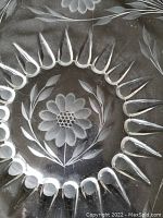 Close-up of cornflower 'Radiance' floral etching on clear glass serving plate showing central flower and radiating teardrop motifs