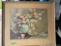 Framed floral print depicting pink and white flowers in a vase with draped fabric background.