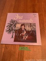 Front cover of the vinyl record 'Ina Naturally' featuring Ina in a car holding a dog, pink background with yellow text.