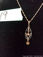 Close-up showing the front of the pendant with detailed decorative filigree, seed pearls, and diamonds.