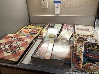 Photo of assortment of vintage cookbooks including Better Homes and Gardens, Mexican cuisine cookbook, and others on a counter.