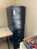 Front view of a black metal file cabinet with four drawers, showing tape residue and marks.