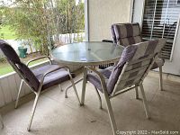 Outdoor patio set showing round metal table with glass top and three cushioned metal chairs with striped cushions.