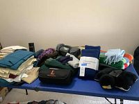 Overview of assorted household linens spread on blue table: multiple blankets, throws, and folded sheets/table linens in various colors and materials.